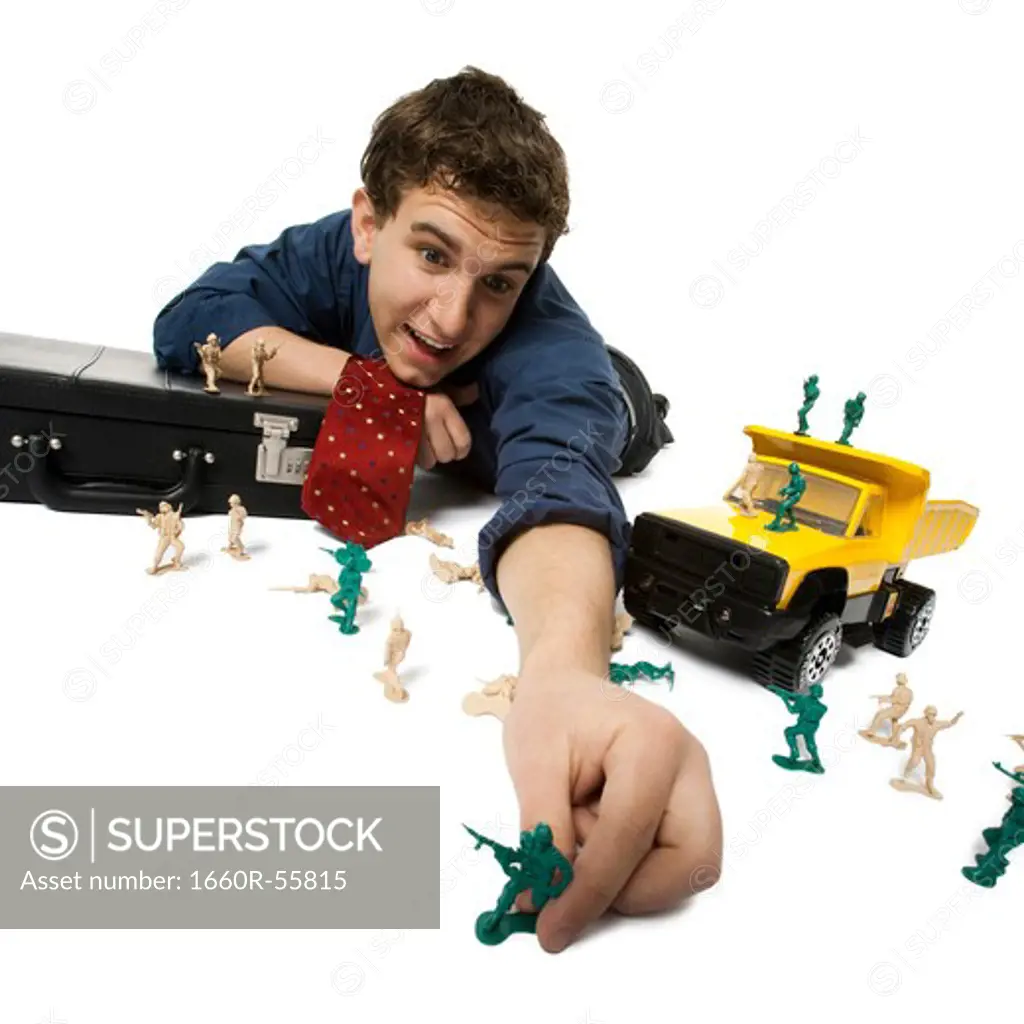 Young businessman playing with plastic army men and truck