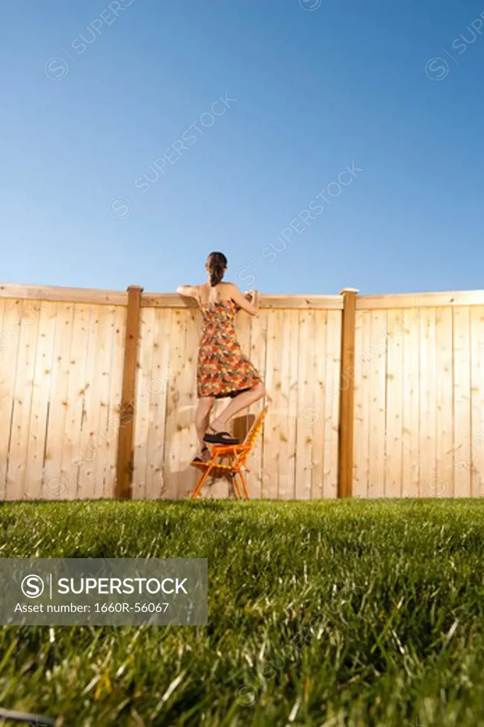 Woman standing on chair peeping over fence