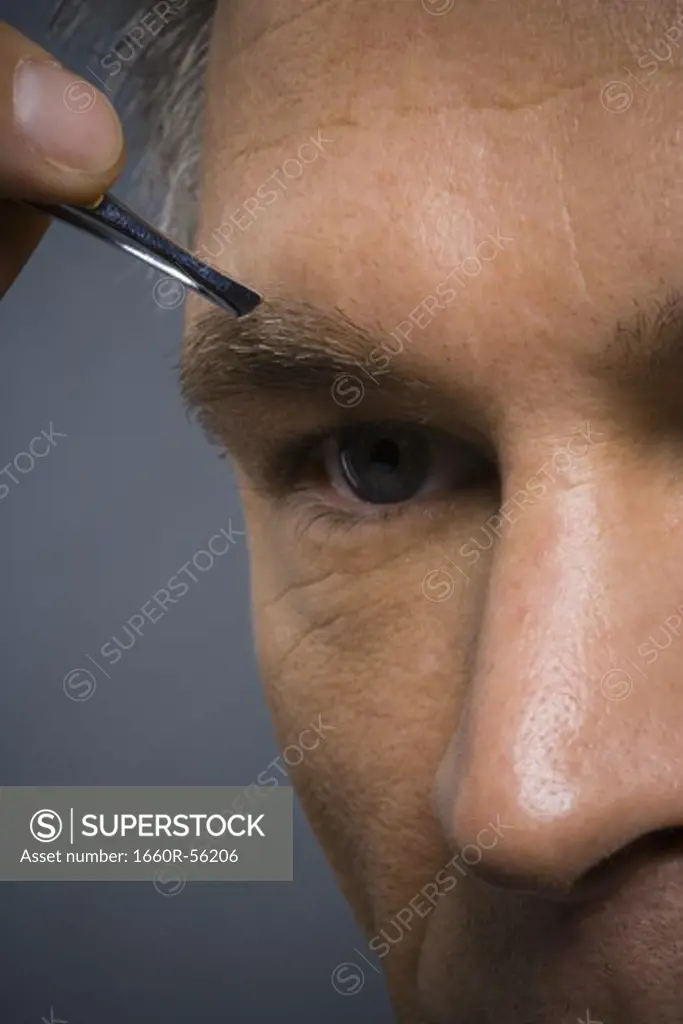 Closeup of man with tweezers plucking eyebrows