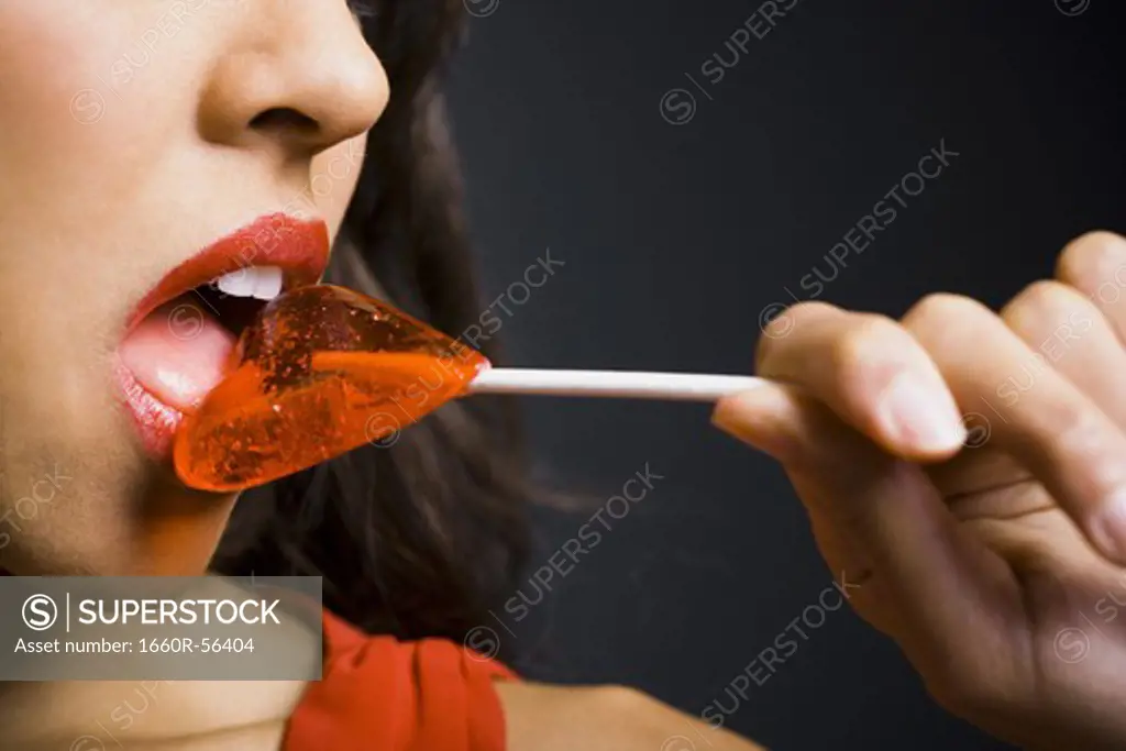 Woman licking heart shaped lollipop closeup