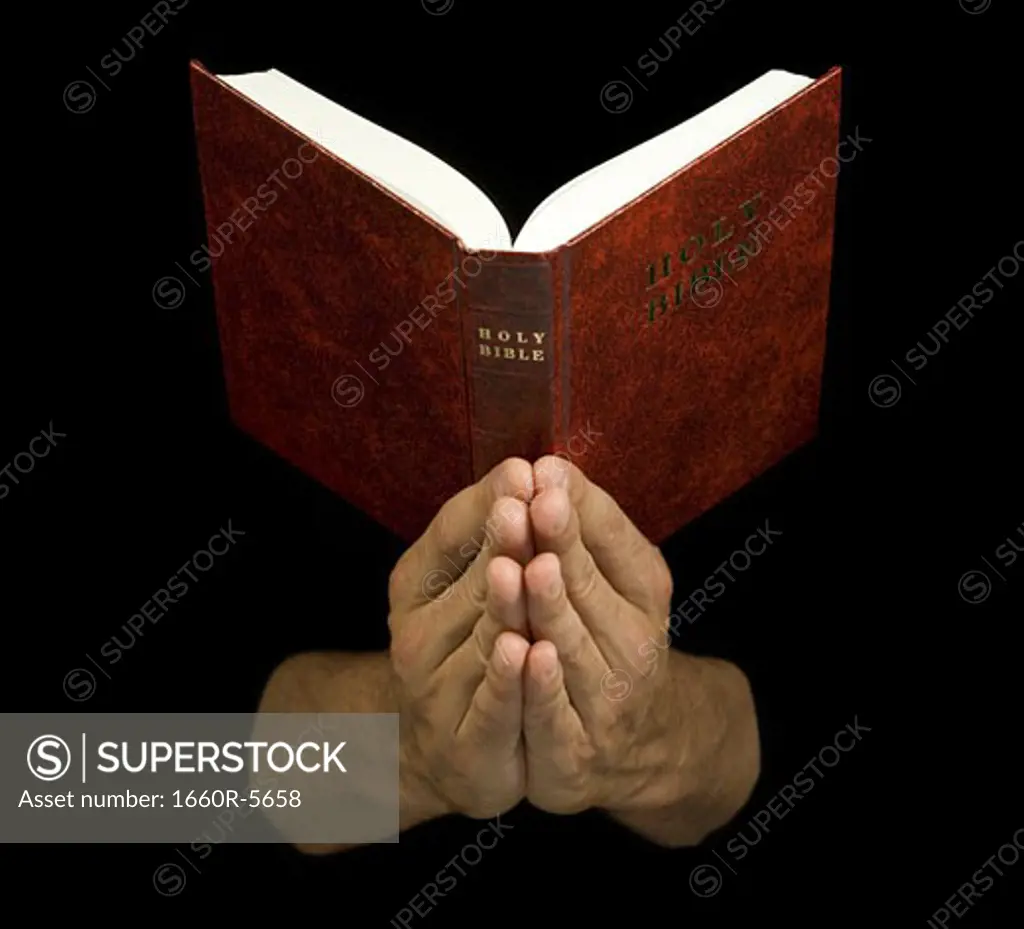 Close-up of a praying hands holding a Bible
