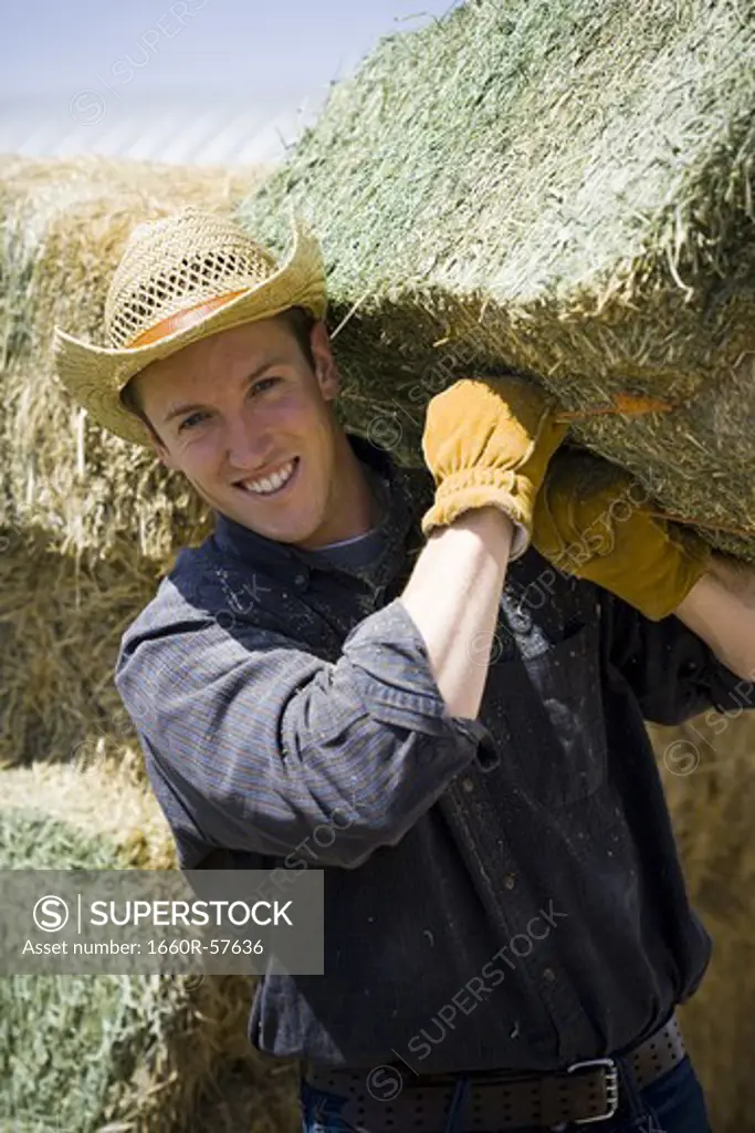 Man in cowboy hat carrying bales of hay smiling