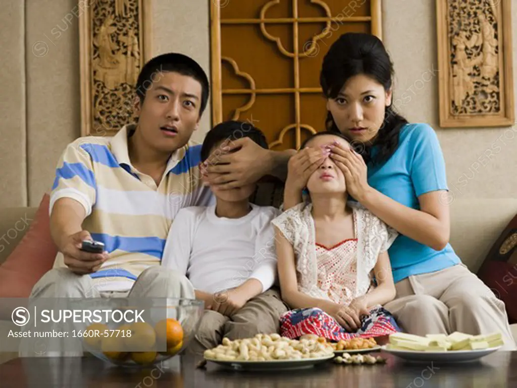 Family watching television with parents covering children's eyes