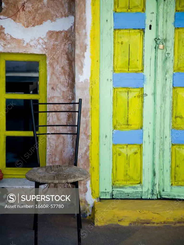 Door painted yellow blue and green with window and empty chair