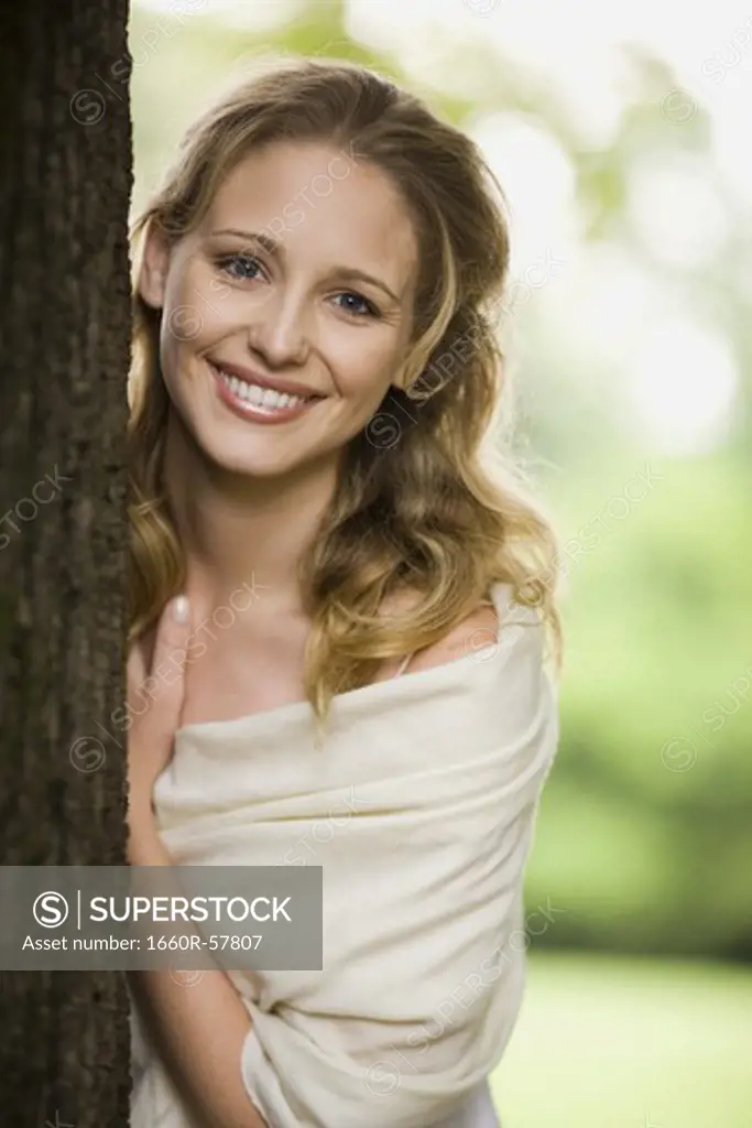 Woman leaning against a tree outdoors smiling