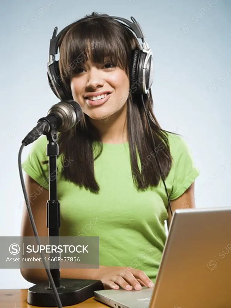 Woman with headphones and laptop singing into microphone