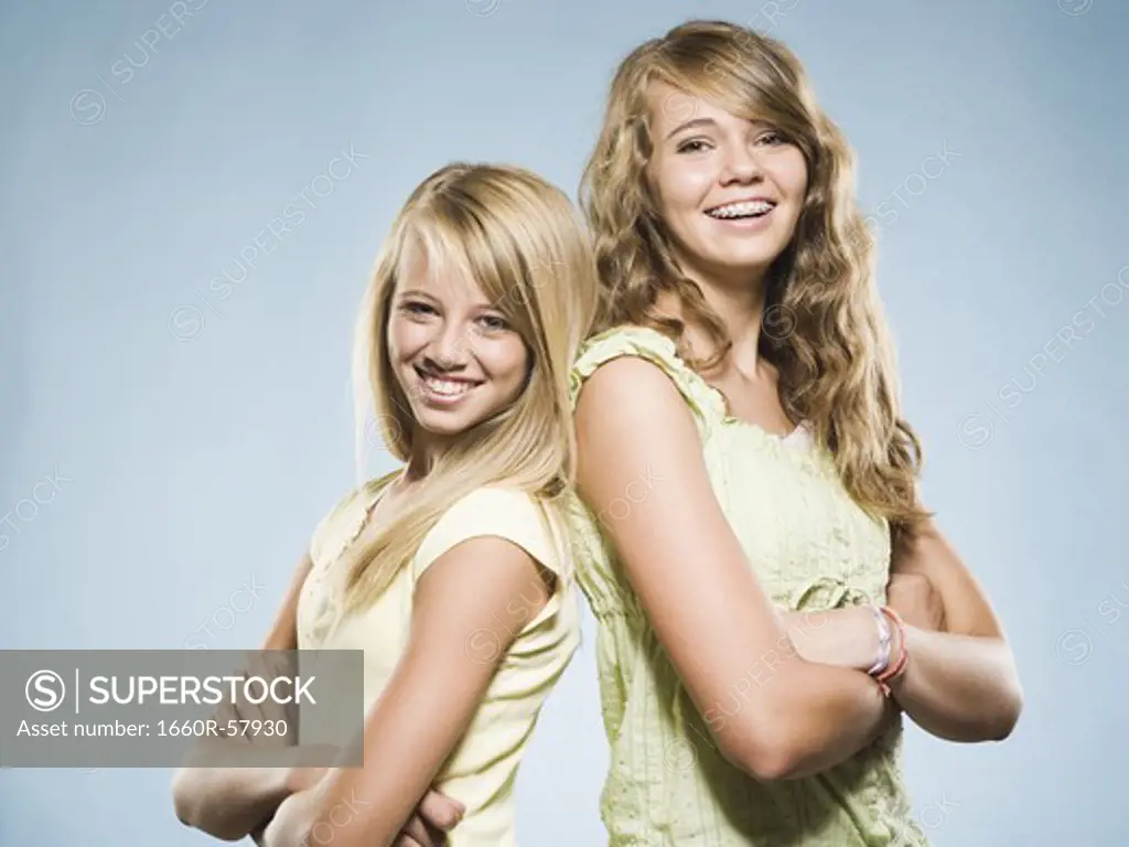 Two girls smiling with arms crossed back to back