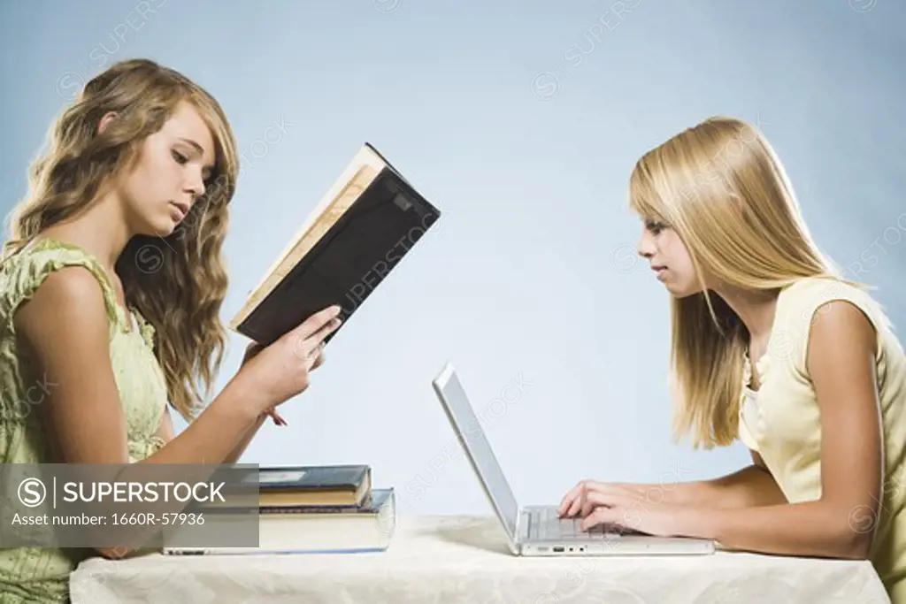 Girl with laptop and girl reading hardcover book