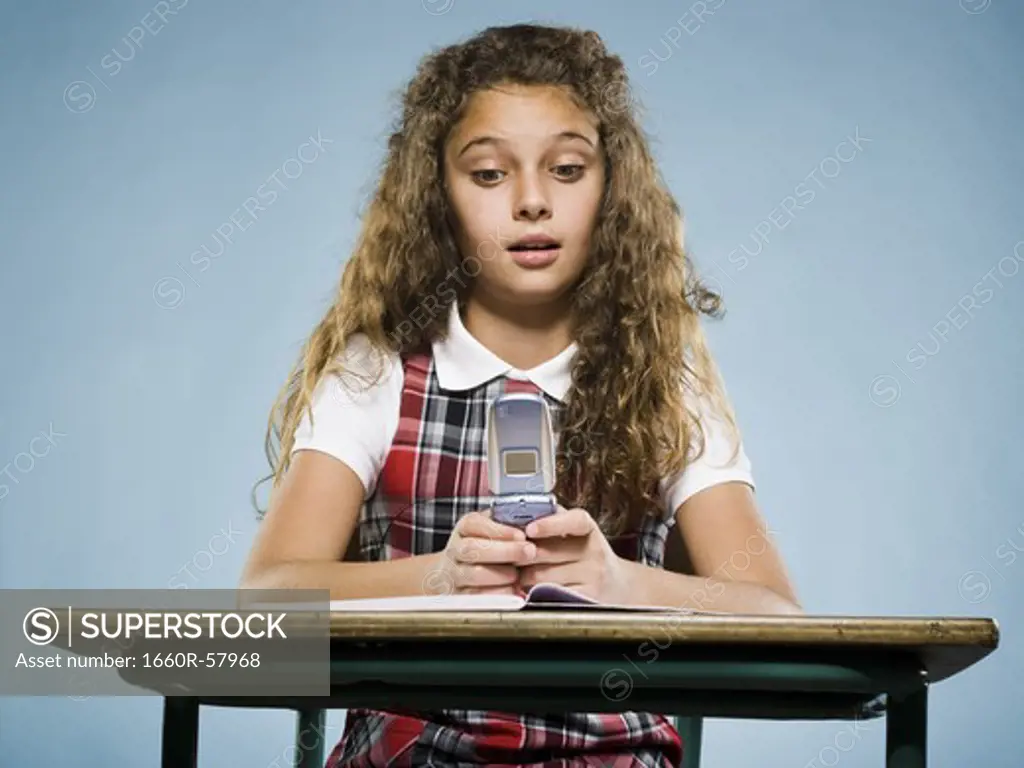 Girl sitting at desk with workbook and cell phone