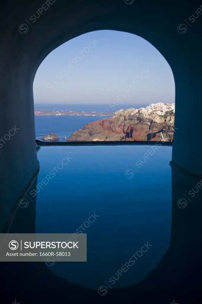 View of infinity pool through archway with mountains and water
