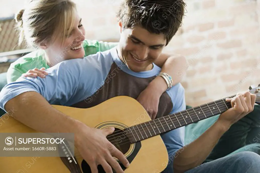 Teenage boy playing a guitar with a teenage girl embracing him