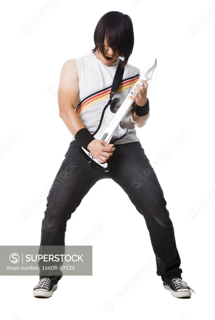 Young man playing guitar video game and screaming, studio shot