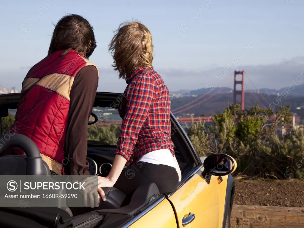 USA, San Francisco, California, young couple sitting in convertible car and looking at Golden Gate Bridge in distance