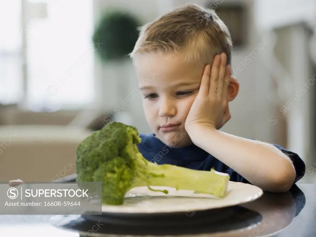 USA, Utah, Alpine, boy (6-7) resting cheek on hand by plate of broccoli
