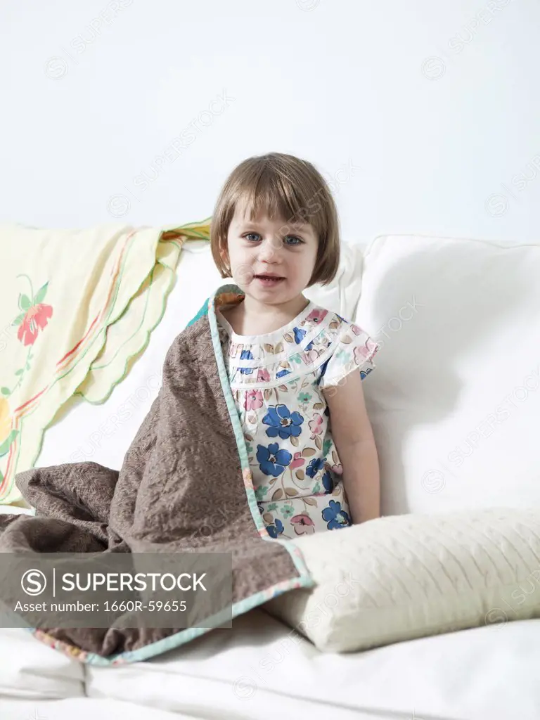 USA, California, San Francisco, girl (2-3) sitting on sofa covered with blanket