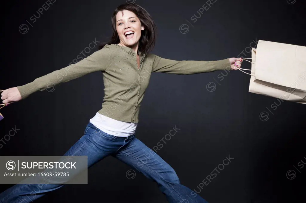 Studio portrait of young woman jumping with shopping bags