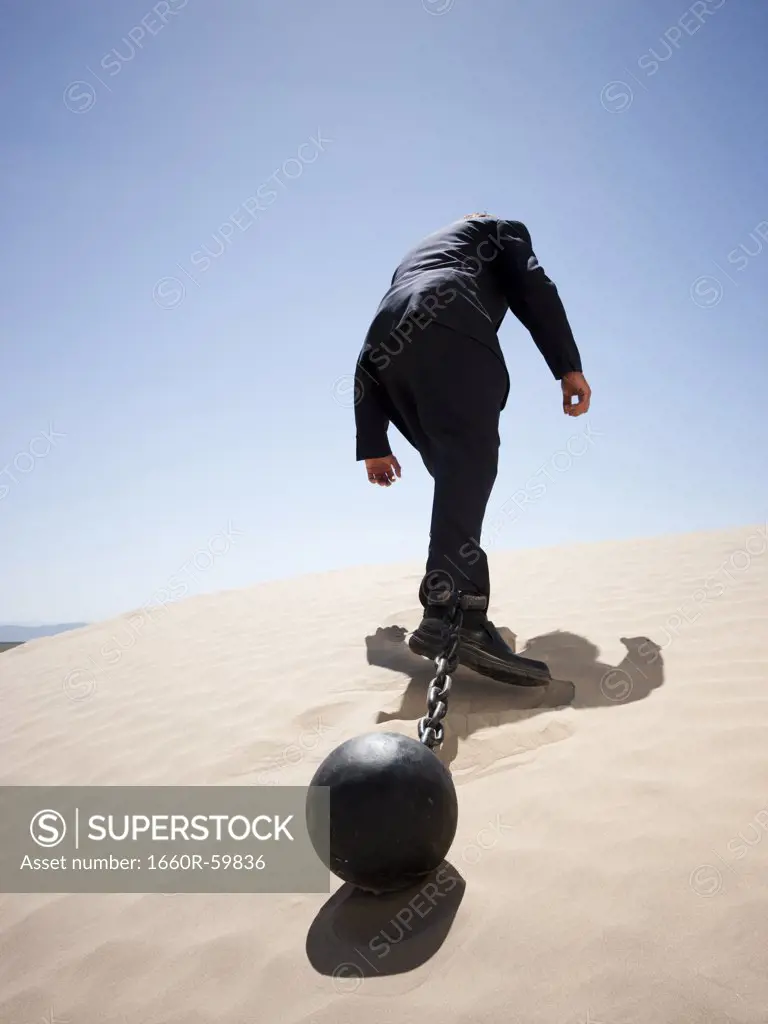 USA, Utah, Little Sahara, mid adult businessman pulling ball in chain on desert, rear view, low angle view