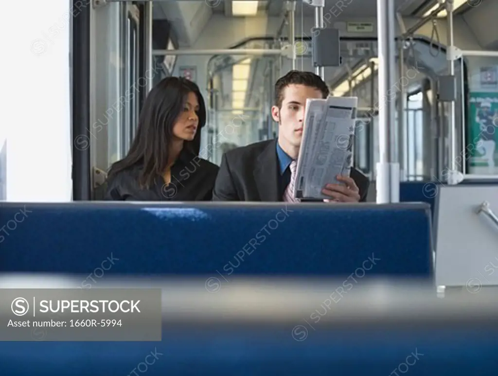 Young man and a young woman reading a newspaper in a train