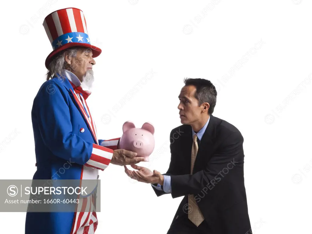 Man in Uncle Sam's costume giving piggybank to other man, studio shot