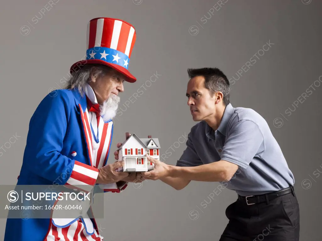 Man in Uncle Sam's costume giving model of house to other man, studio shot