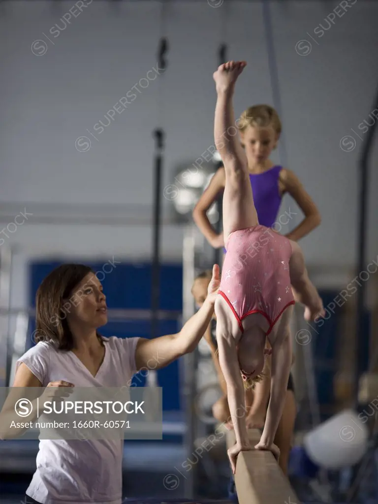 USA, Utah, Orem, Instructor helping gymnasts (6-9) to perform handstand on beam