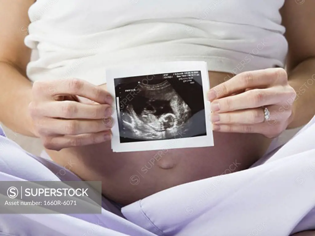 Mid section view of a pregnant woman holding a sonogram of her baby