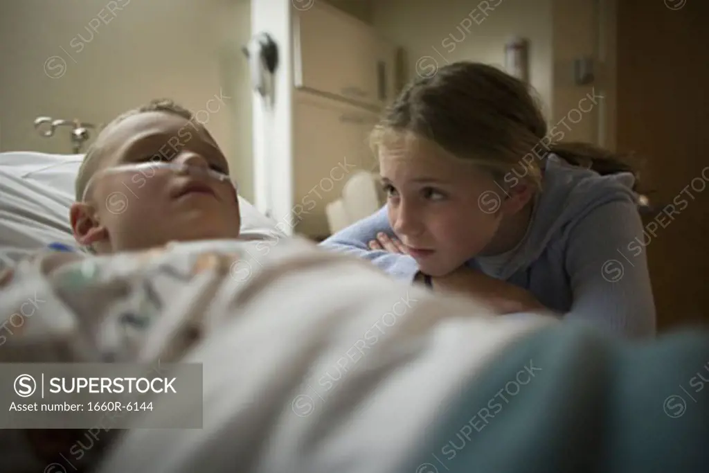 Sister looking at her brother lying in a hospital bed