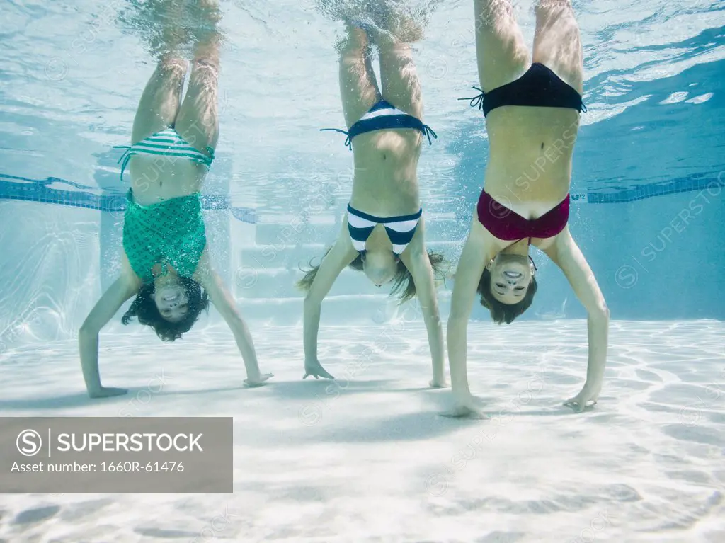 teenagers in a swimming pool doing handstands under water