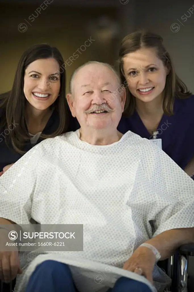 Portrait of two female nurses helping a male patient sitting on a wheel chair