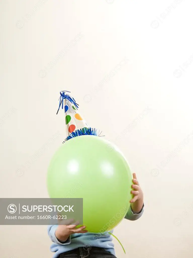 child wearing a party hat holding a balloon in front of his face