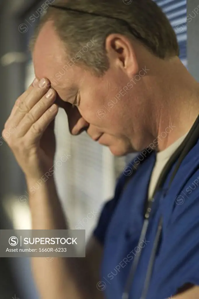 Close-up of a male doctor with his hand on his forehead