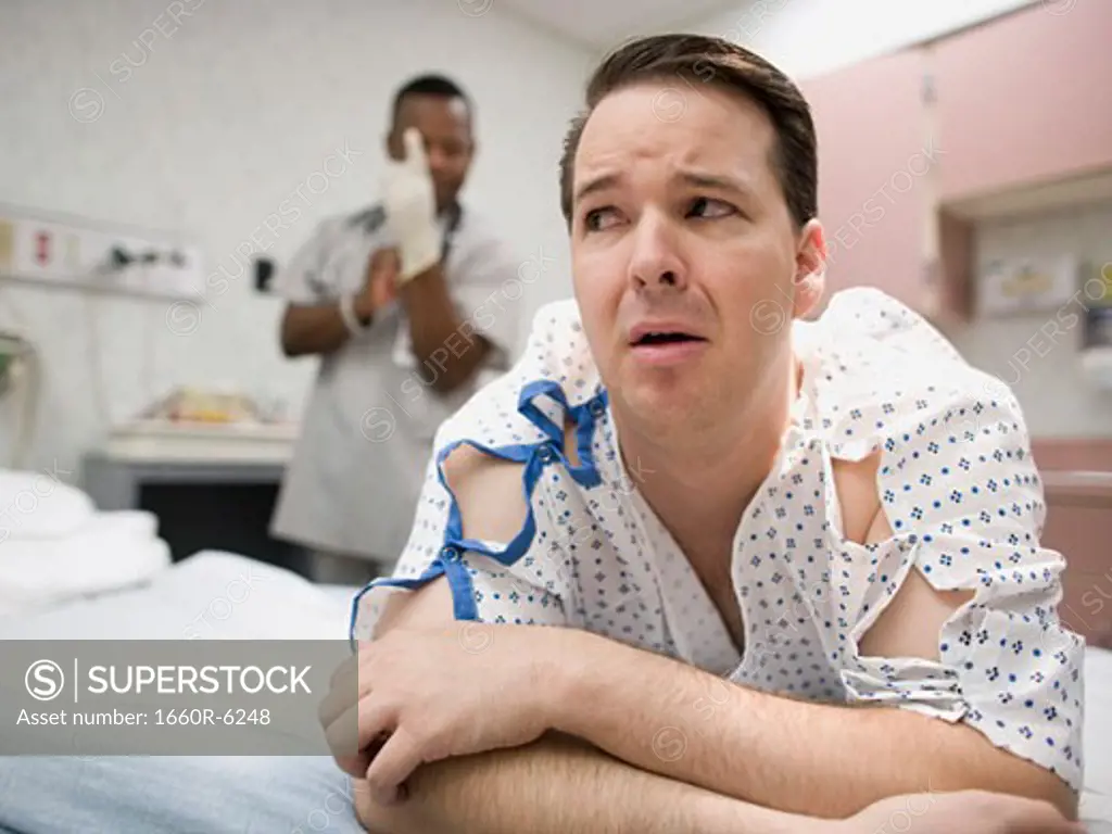 A nervous patient lying on the bed with a doctor putting on latex gloves in the background