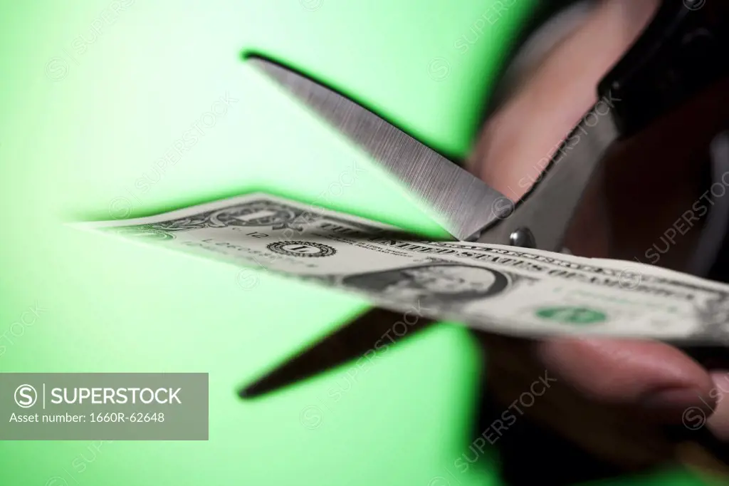 Hand with scissors cutting US dollar bill