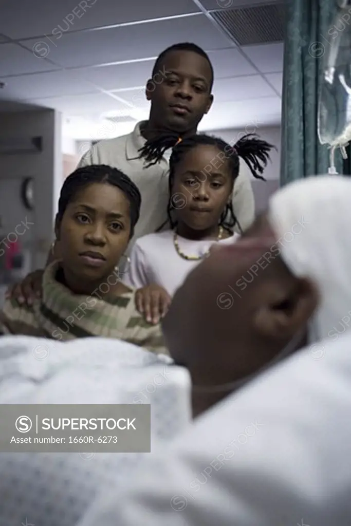 Parents and their daughter looking at a teenage boy in the hospital