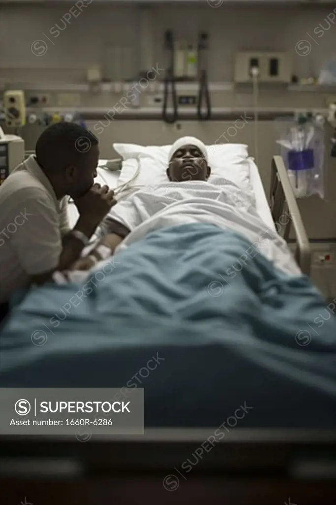 Profile of a father sitting beside his son lying on a hospital bed