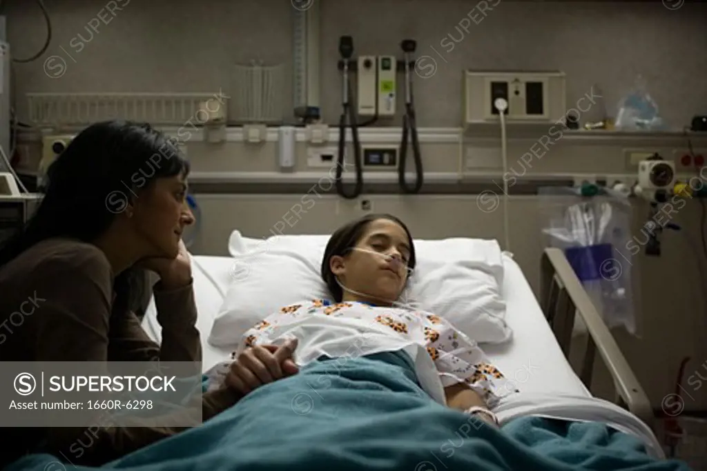 Daughter lying on a hospital bed with her mother holding her hand