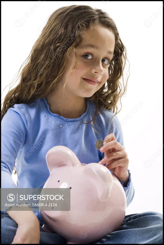 Young girl depositing money in piggy bank