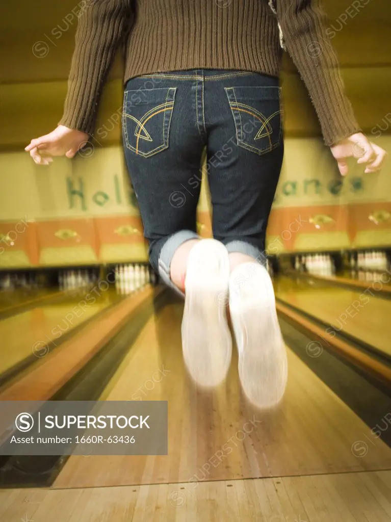 Rear view of a teenage girl jumping in a bowling alley