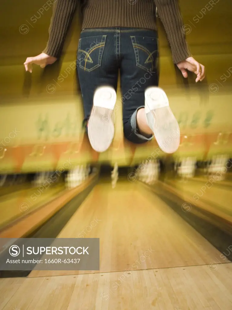 Rear view of a teenage girl jumping in a bowling alley