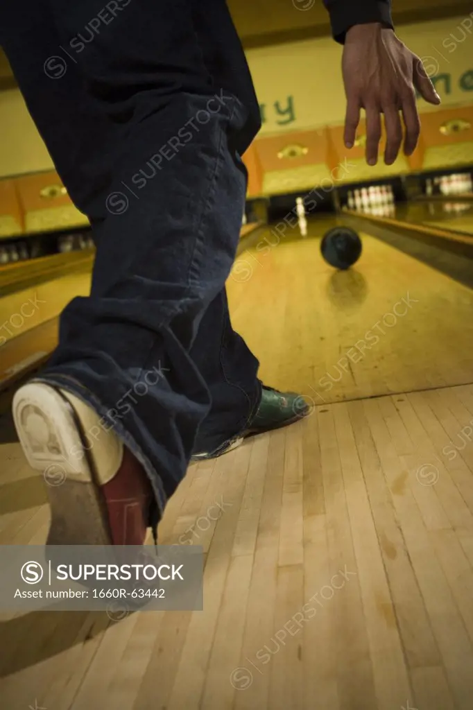 Low section view of a young man bowling at a bowling alley