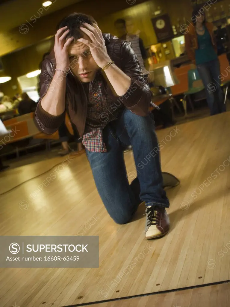 Young man kneeling with his hand on his forehead at a bowling alley