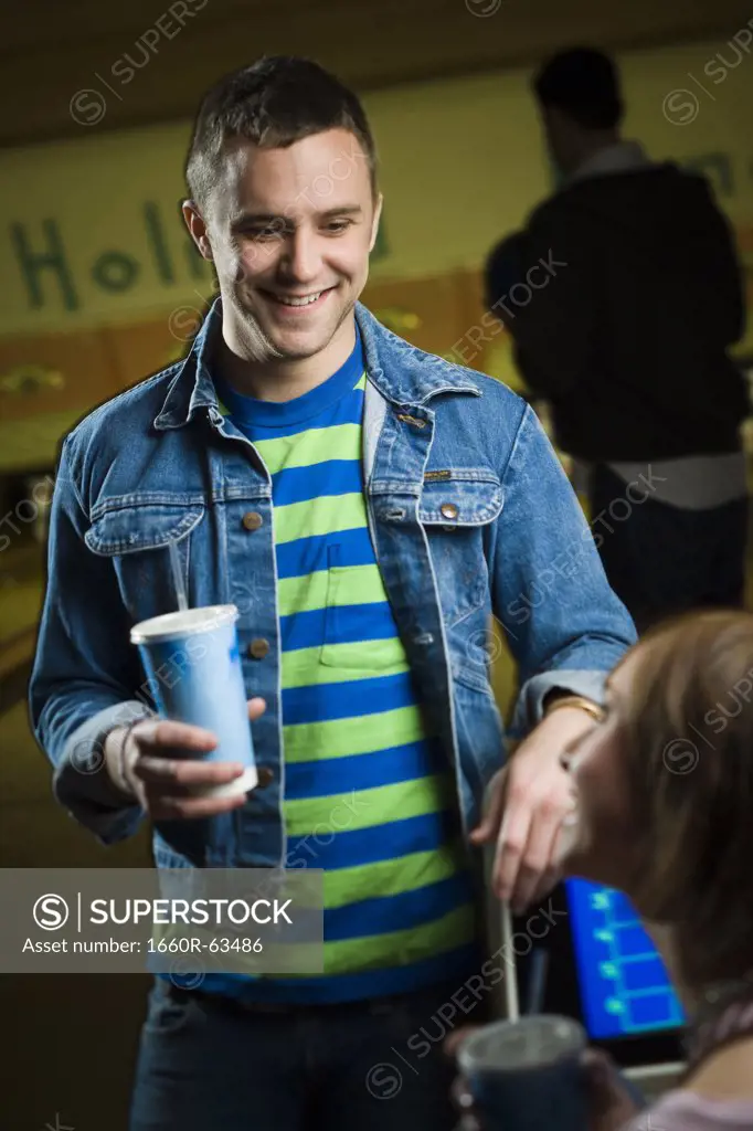 Young man and a teenage girl holding glasses of cola and looking at each other
