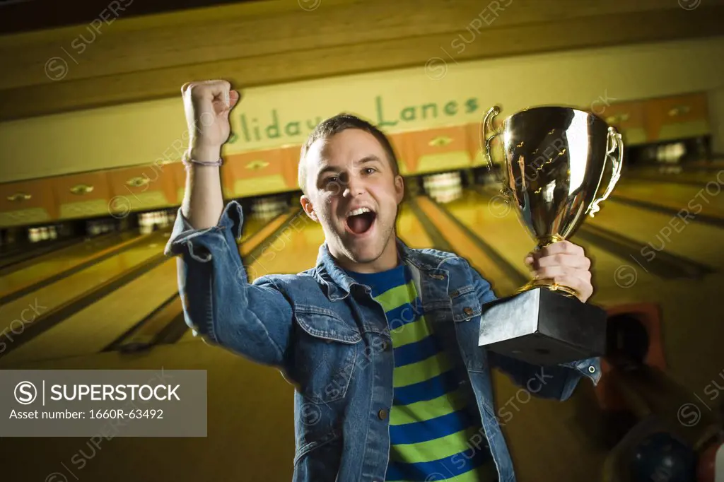 Portrait of a young man holding a bowling trophy and gesturing with his hand