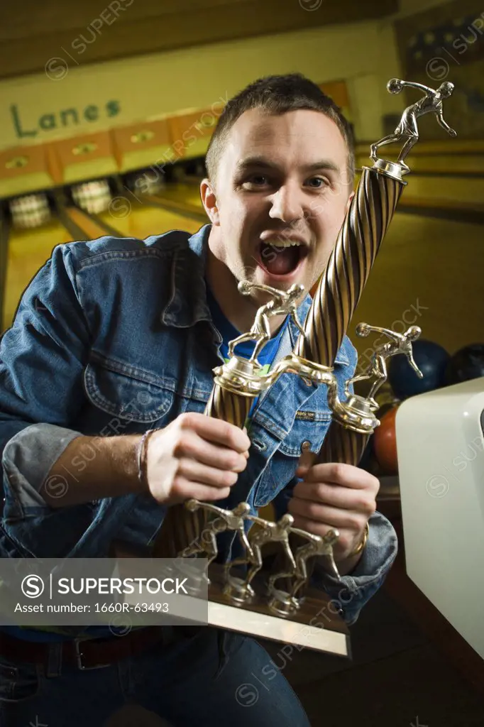 Portrait of a young man holding a bowling trophy and dancing
