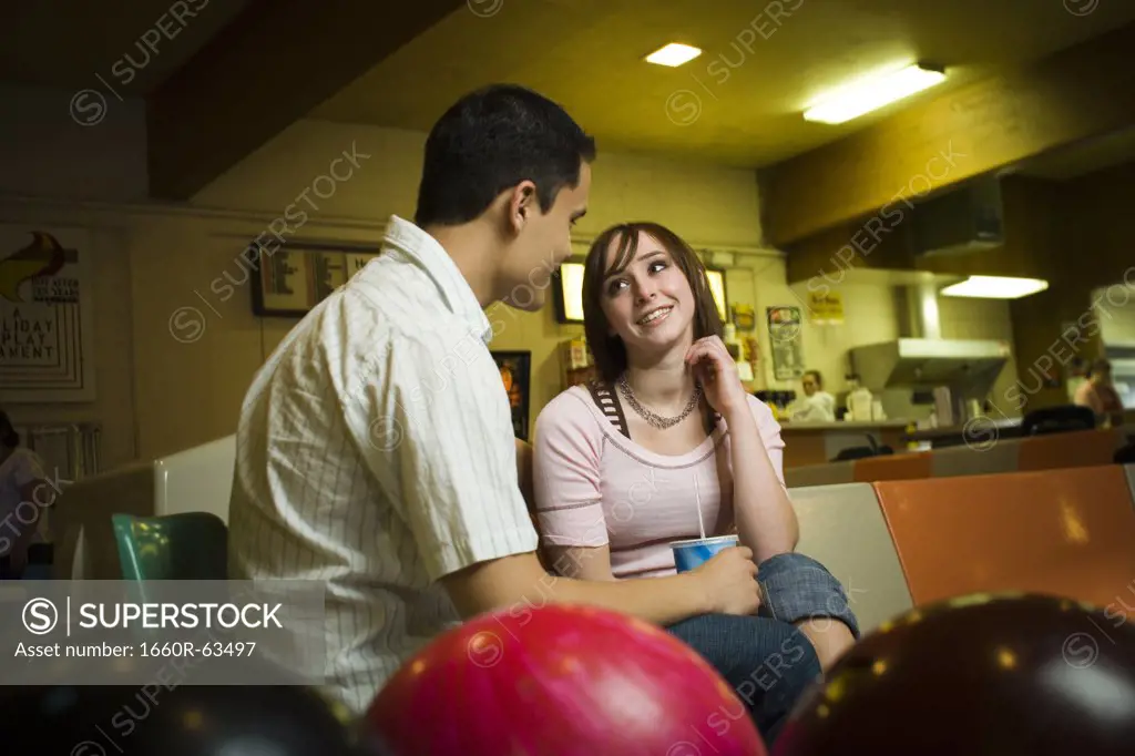 Low angle view of a young man sitting with a teenage girl in a bowling alley