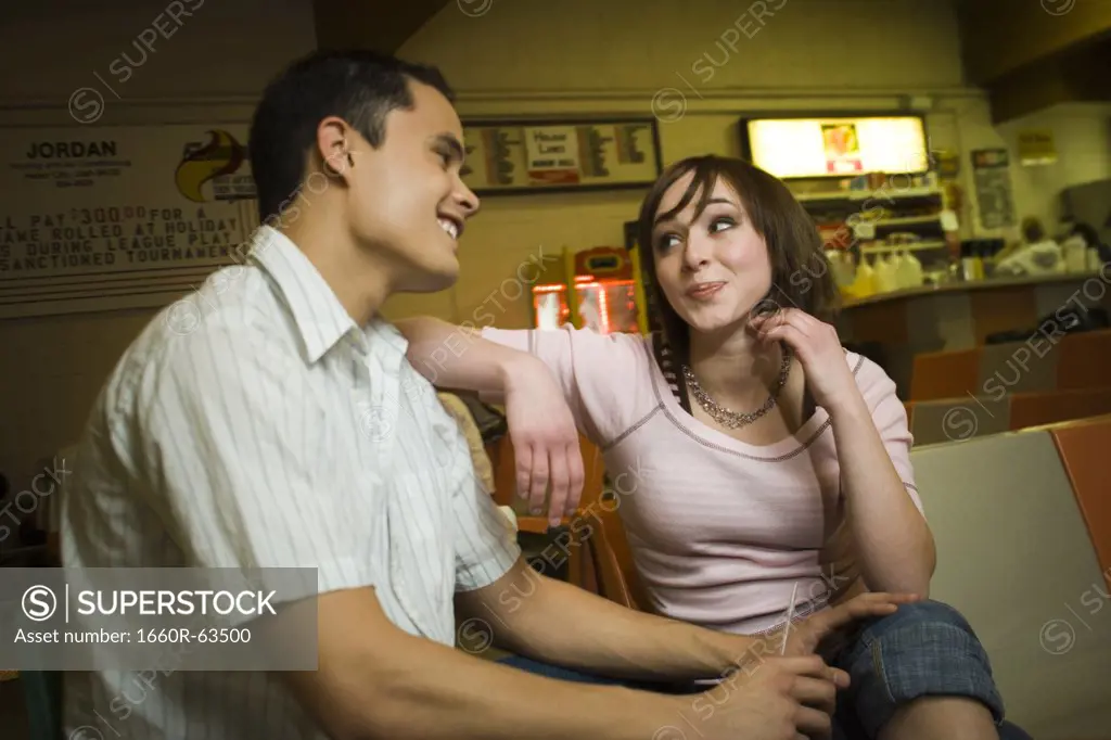 Low angle view of a young man sitting with a teenage girl in a bowling alley