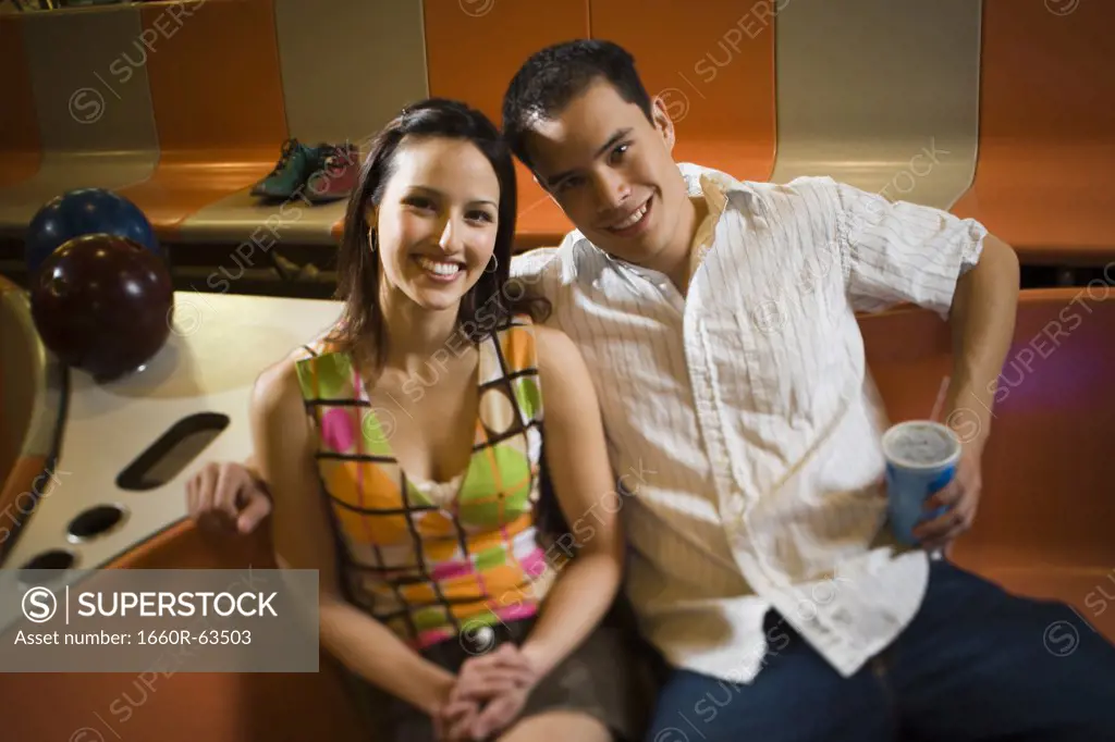 Portrait of a young man and a teenage girl sitting in a bowling alley