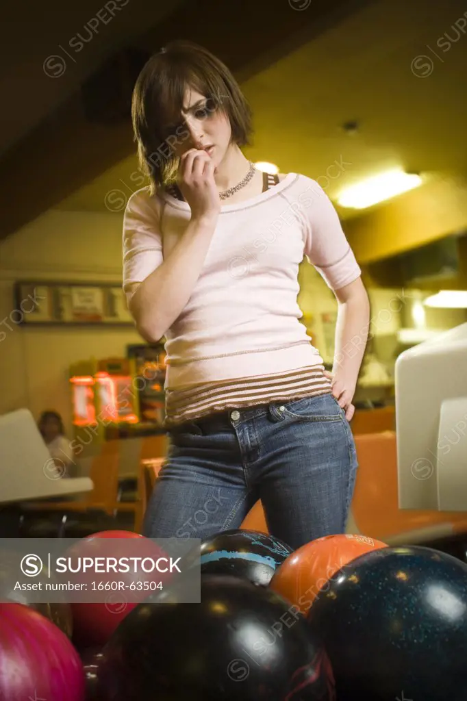 Low angle view of a teenage girl looking at bowling balls and scratching her head