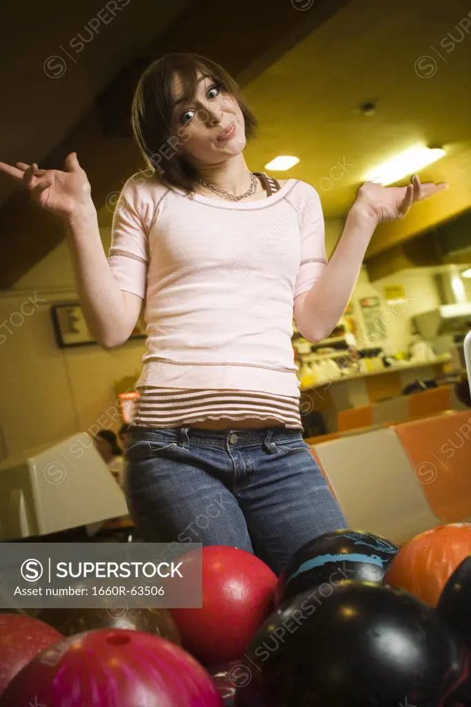Low angle view of a teenage girl looking at bowling balls and scratching her head