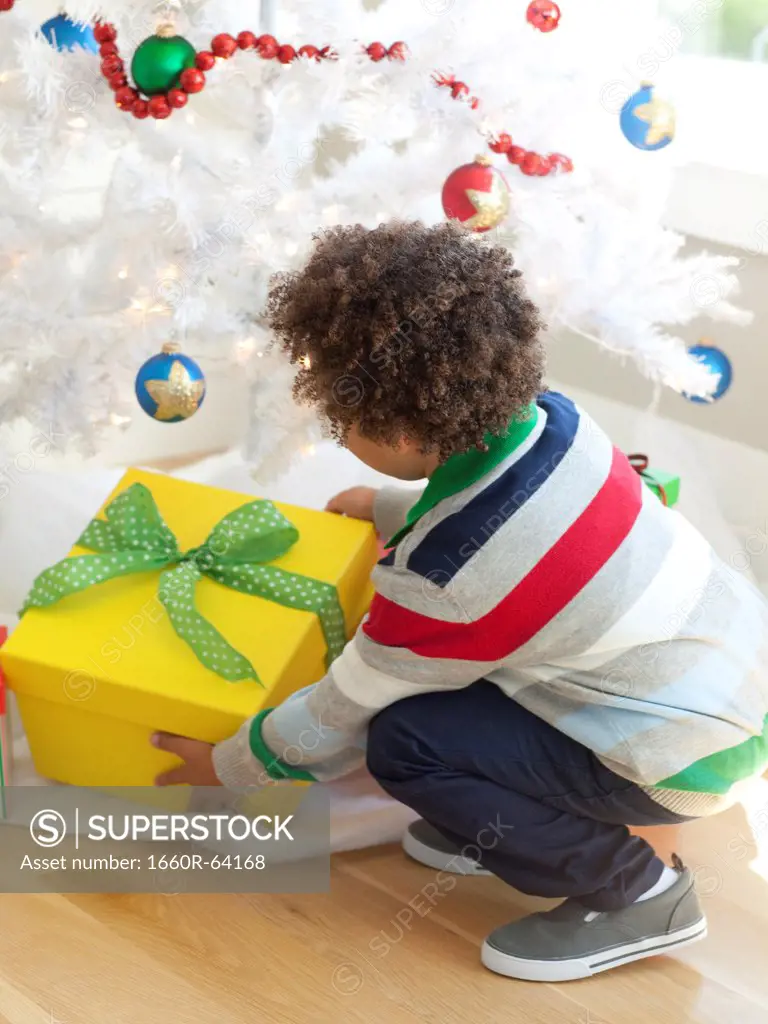 Young boy picking up Christmas present from under Christmas tree